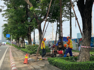 Công nhân khoan khảo sát địa chất trên vỉa hè khu vực Thủ Thiêm, phía sau là công trường đang thi công